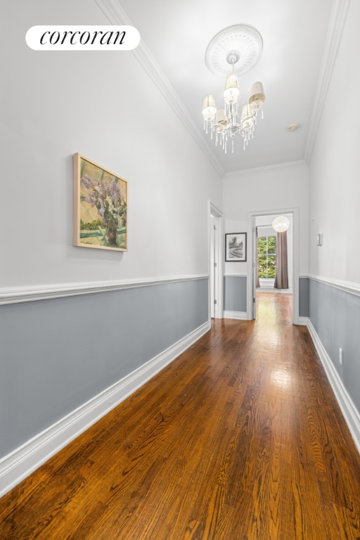 unfurnished living room with wood-type flooring, crown molding, and a chandelier