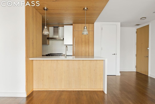 kitchen with pendant lighting, wall chimney range hood, decorative backsplash, sink, and kitchen peninsula