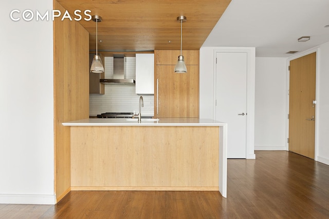 kitchen with pendant lighting, dark wood-style flooring, backsplash, a sink, and wall chimney range hood