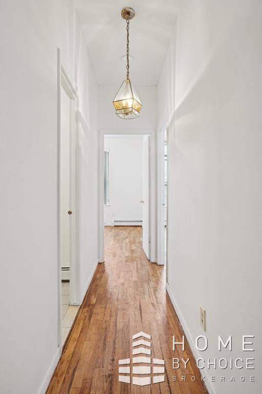 corridor with light hardwood / wood-style floors and a baseboard heating unit