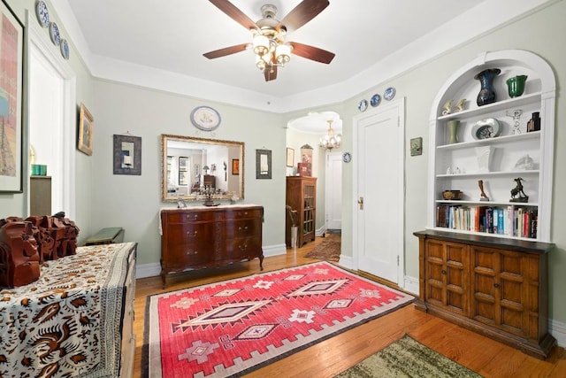 sitting room with built in features, ceiling fan with notable chandelier, and light hardwood / wood-style floors