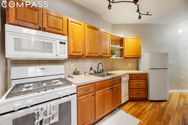 kitchen featuring light wood-type flooring, a sink, tasteful backsplash, white appliances, and light countertops