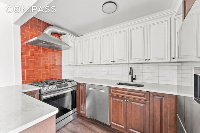 kitchen with white cabinets, dark wood-style flooring, stainless steel appliances, wall chimney range hood, and a sink