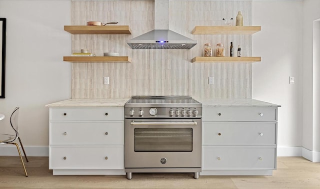 kitchen with high end stove, light hardwood / wood-style flooring, light stone countertops, white cabinets, and wall chimney exhaust hood