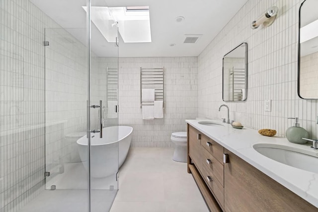 full bathroom with tile patterned floors, vanity, a skylight, tile walls, and toilet