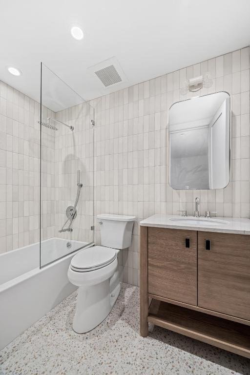 full bathroom featuring toilet, tile walls, tiled shower / bath, and vanity