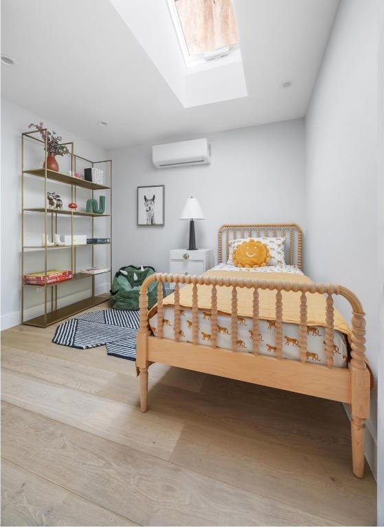 bedroom featuring hardwood / wood-style flooring, a skylight, and a wall mounted AC