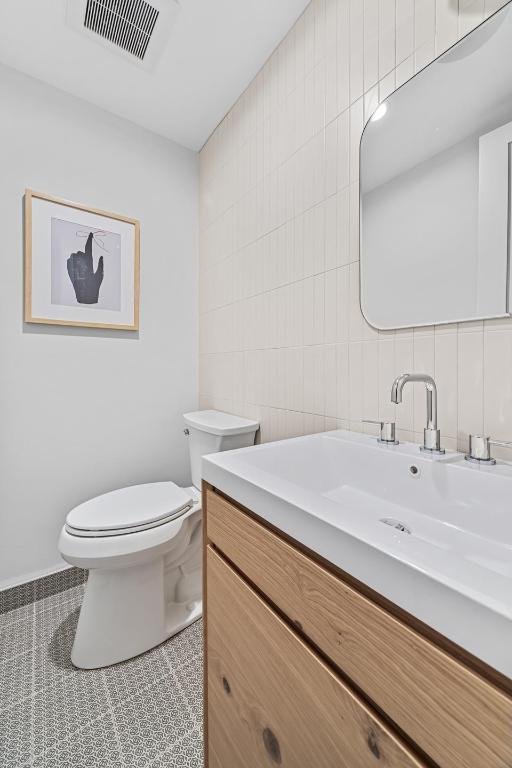 bathroom featuring tile patterned flooring, vanity, decorative backsplash, tile walls, and toilet