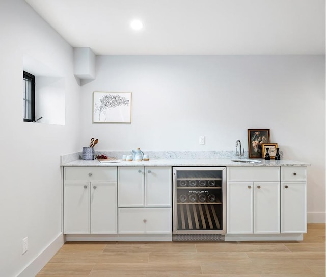 bar with light stone counters, sink, white cabinetry, and wine cooler