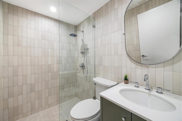 bathroom with toilet, a tile shower, tile walls, and vanity