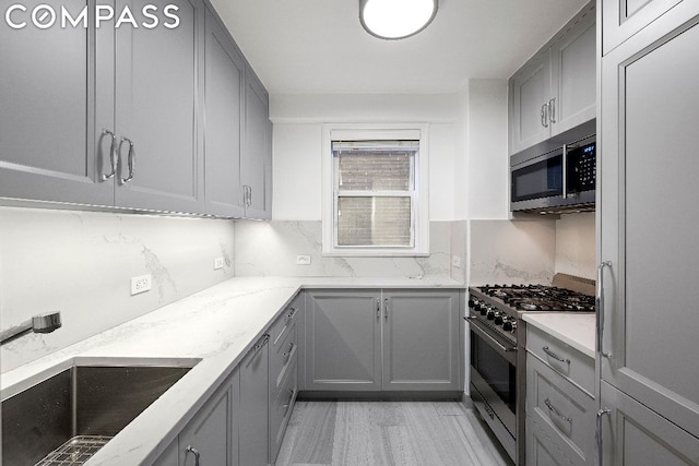 kitchen featuring tasteful backsplash, sink, appliances with stainless steel finishes, gray cabinetry, and light stone counters