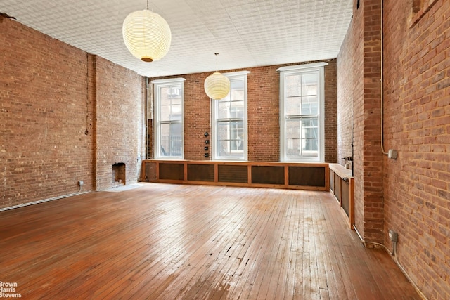 empty room featuring brick wall, wood-type flooring, and a large fireplace