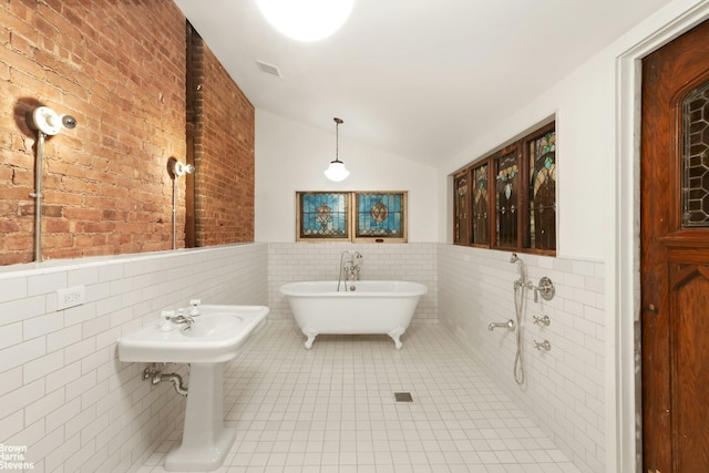 bathroom with brick wall, lofted ceiling, tile walls, a tub to relax in, and tile patterned floors