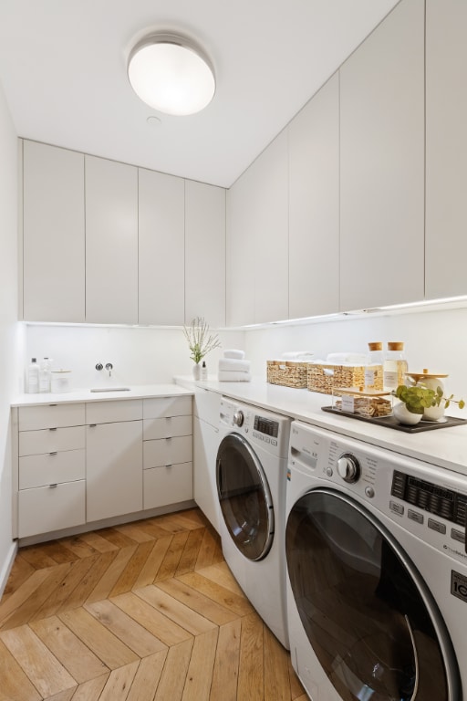 washroom featuring light parquet flooring, washing machine and dryer, and cabinets