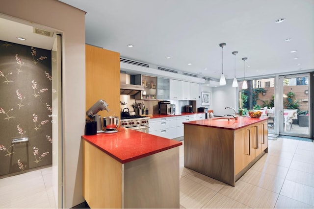 kitchen with pendant lighting, white cabinetry, an island with sink, high end stainless steel range, and a wall of windows