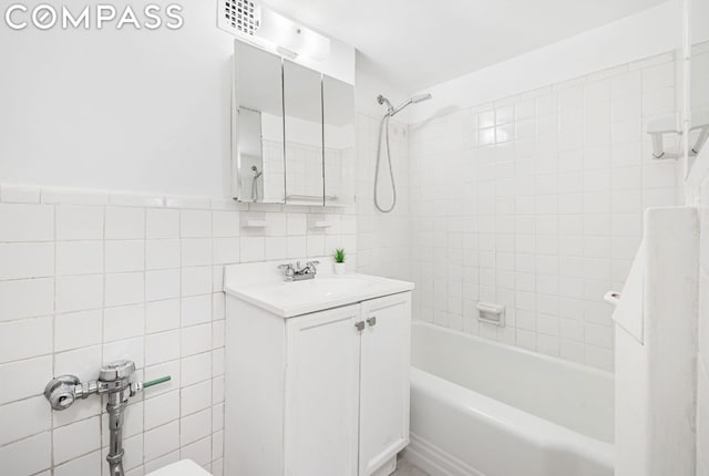 bathroom with tiled shower / bath, tile walls, and vanity