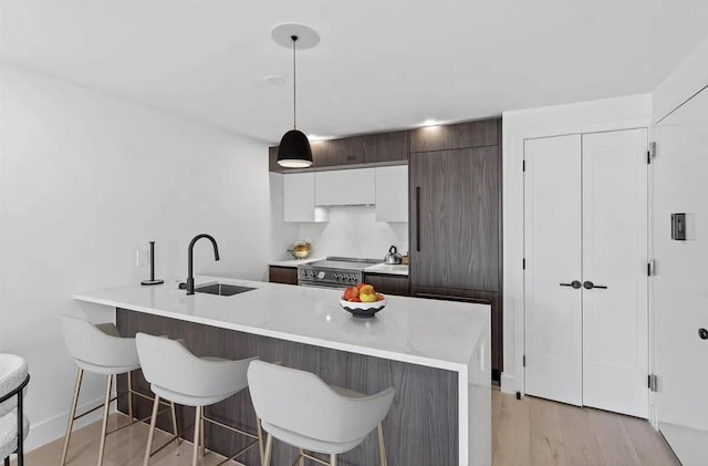 kitchen with decorative light fixtures, kitchen peninsula, sink, white cabinetry, and dark brown cabinets