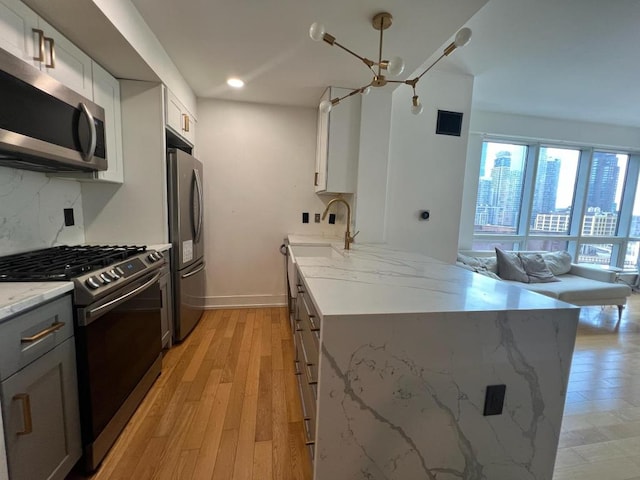 kitchen with light hardwood / wood-style floors, stainless steel appliances, gray cabinetry, white cabinets, and light stone counters