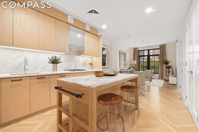 kitchen featuring light parquet flooring, wall chimney range hood, a kitchen island, sink, and light brown cabinetry