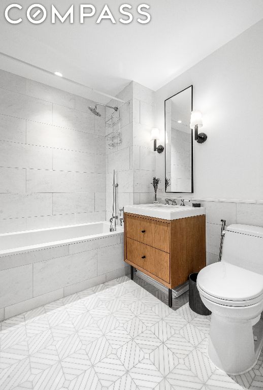 full bathroom featuring tile walls, tiled shower / bath combo, vanity, and toilet