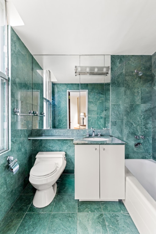 bathroom featuring toilet, tile walls, a bath, and vanity