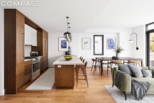 kitchen with a center island, hanging light fixtures, light wood-type flooring, gas range, and a breakfast bar