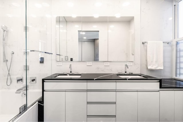 bathroom with a sink, shower / bath combination with glass door, and double vanity