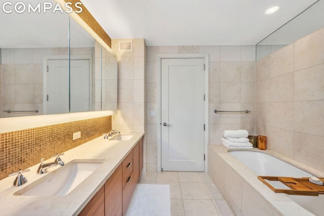 bathroom featuring a relaxing tiled tub, tile walls, vanity, and tile patterned flooring