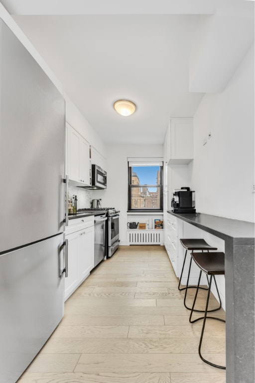 kitchen featuring white cabinetry, appliances with stainless steel finishes, tasteful backsplash, a kitchen breakfast bar, and light hardwood / wood-style flooring