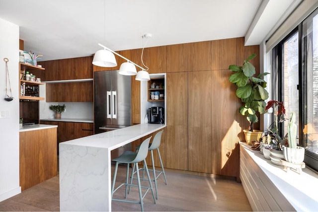 kitchen featuring a breakfast bar, hanging light fixtures, kitchen peninsula, high end fridge, and light hardwood / wood-style flooring