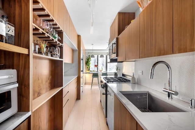 kitchen with sink, light hardwood / wood-style flooring, appliances with stainless steel finishes, backsplash, and decorative light fixtures