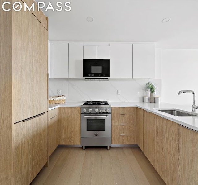 kitchen with backsplash, sink, white cabinetry, light hardwood / wood-style flooring, and stainless steel range