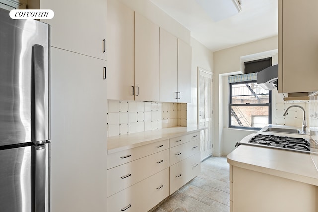 kitchen featuring a sink, light countertops, backsplash, and freestanding refrigerator