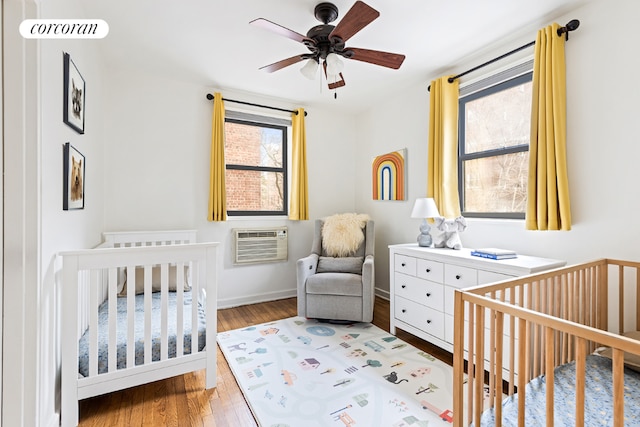 bedroom featuring ceiling fan, wood-type flooring, a crib, and a wall mounted air conditioner