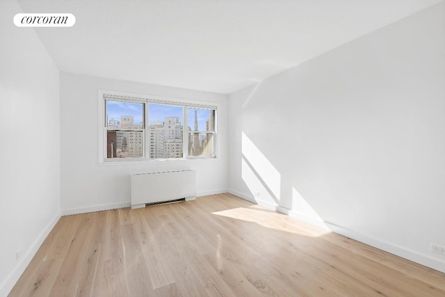 empty room featuring light wood-type flooring and radiator heating unit