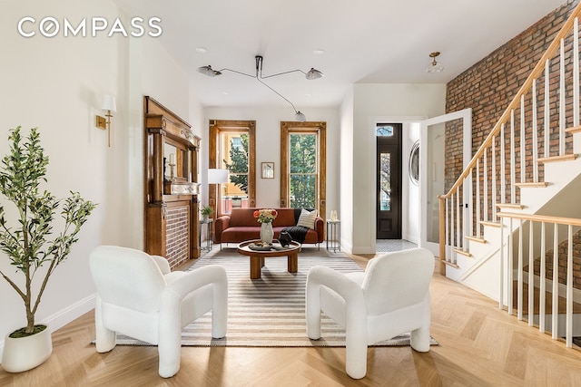 living area featuring brick wall, baseboards, and stairs