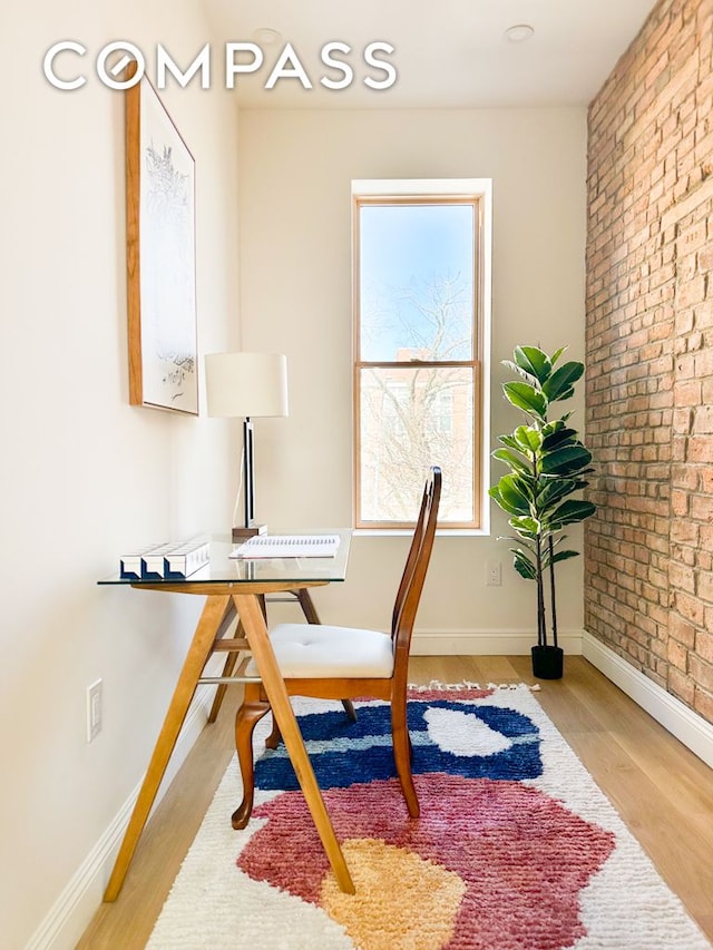 office space featuring light wood-style floors, baseboards, and brick wall