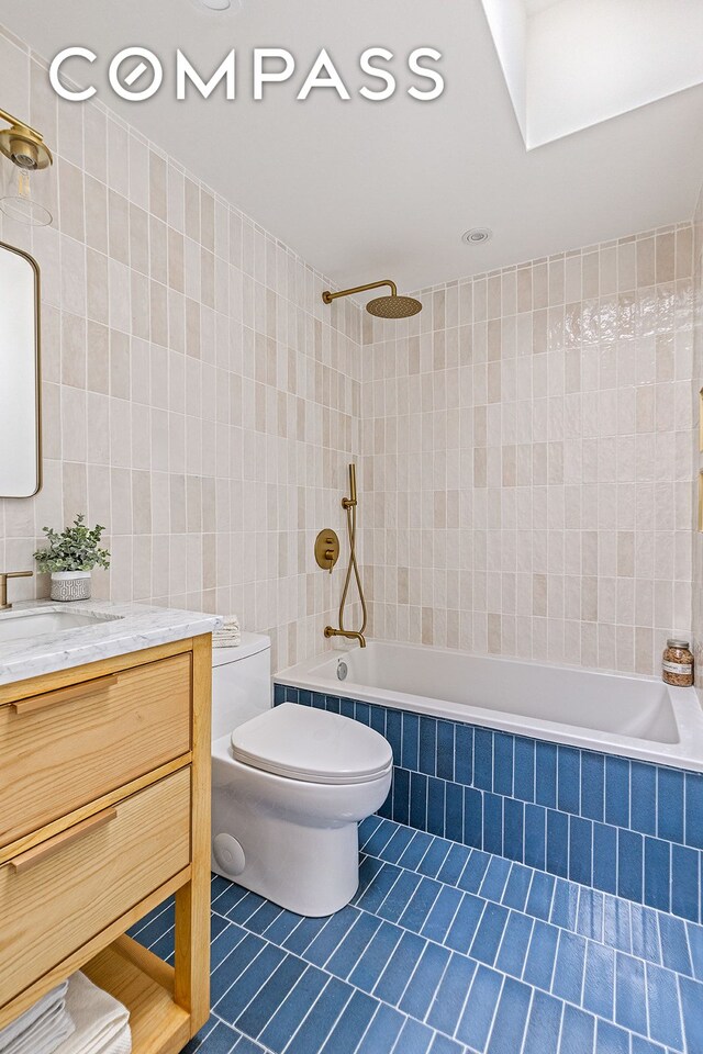 bathroom featuring tile patterned floors, tiled shower / bath, toilet, tile walls, and vanity