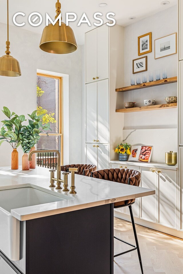 kitchen featuring a sink, breakfast area, white cabinets, light stone countertops, and hanging light fixtures