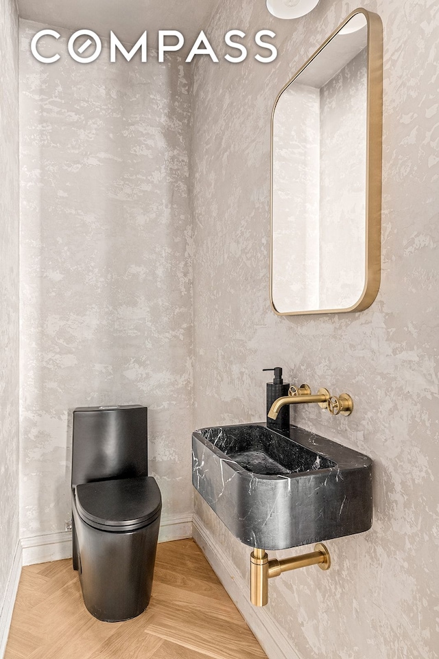 half bath featuring wood finished floors, baseboards, and a sink