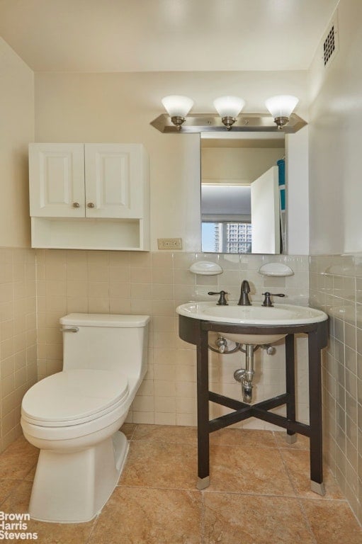 bathroom with toilet, tile walls, and tile patterned floors