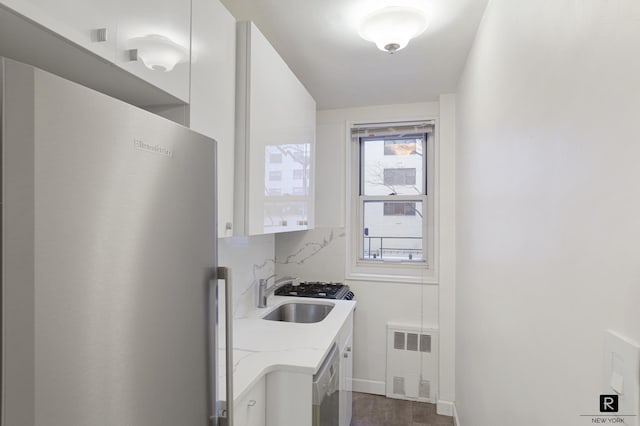 kitchen with tasteful backsplash, radiator heating unit, freestanding refrigerator, white cabinets, and a sink