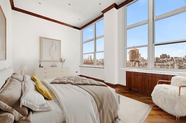 bedroom featuring a view of city, ornamental molding, light wood-style flooring, and baseboards