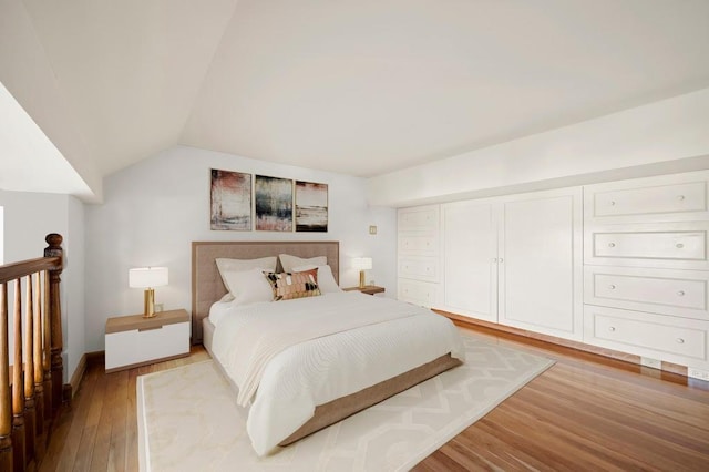 bedroom with light wood-style floors, lofted ceiling, and baseboards