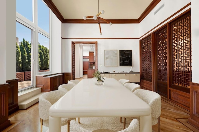 dining space with crown molding, light wood-style flooring, visible vents, and wainscoting