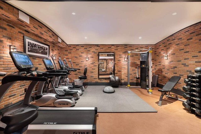 exercise room with vaulted ceiling and brick wall