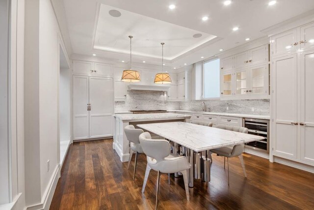 kitchen with hanging light fixtures, wine cooler, a tray ceiling, white cabinets, and a kitchen island