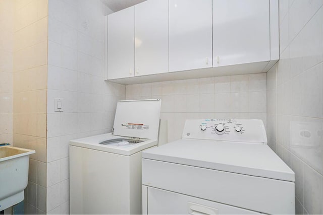 clothes washing area featuring cabinets, sink, tile walls, and independent washer and dryer