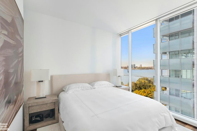 bedroom featuring a water view, hardwood / wood-style floors, and expansive windows