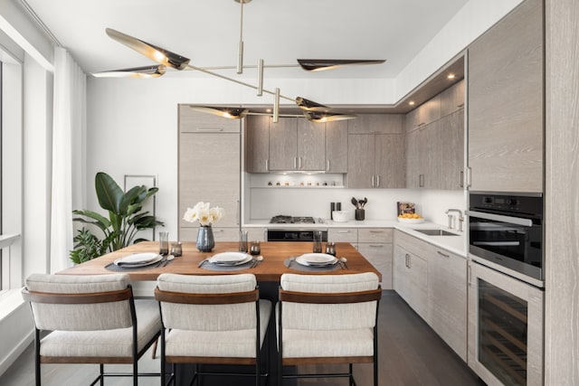 kitchen with ceiling fan, appliances with stainless steel finishes, beverage cooler, a breakfast bar, and sink